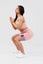 Girl holding squat wearing pink calypso seamless set wearing purple resistance band around thighs