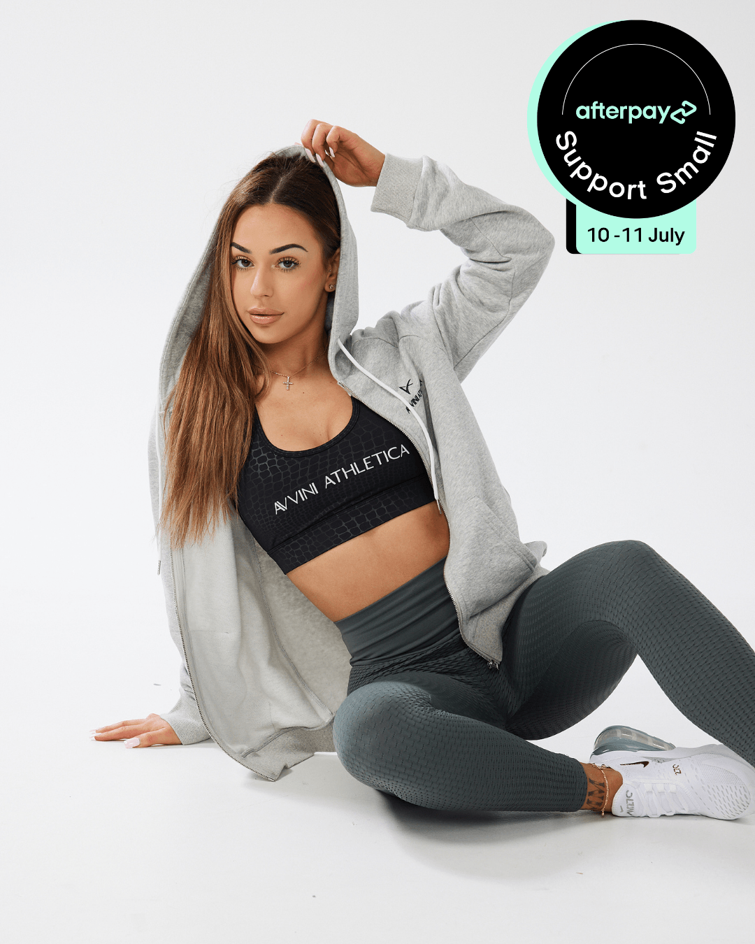 Girl posing on the floor wearing black crop top, grey jack unzipped, khaki luna x leggings with after pay support small logo in top right corner