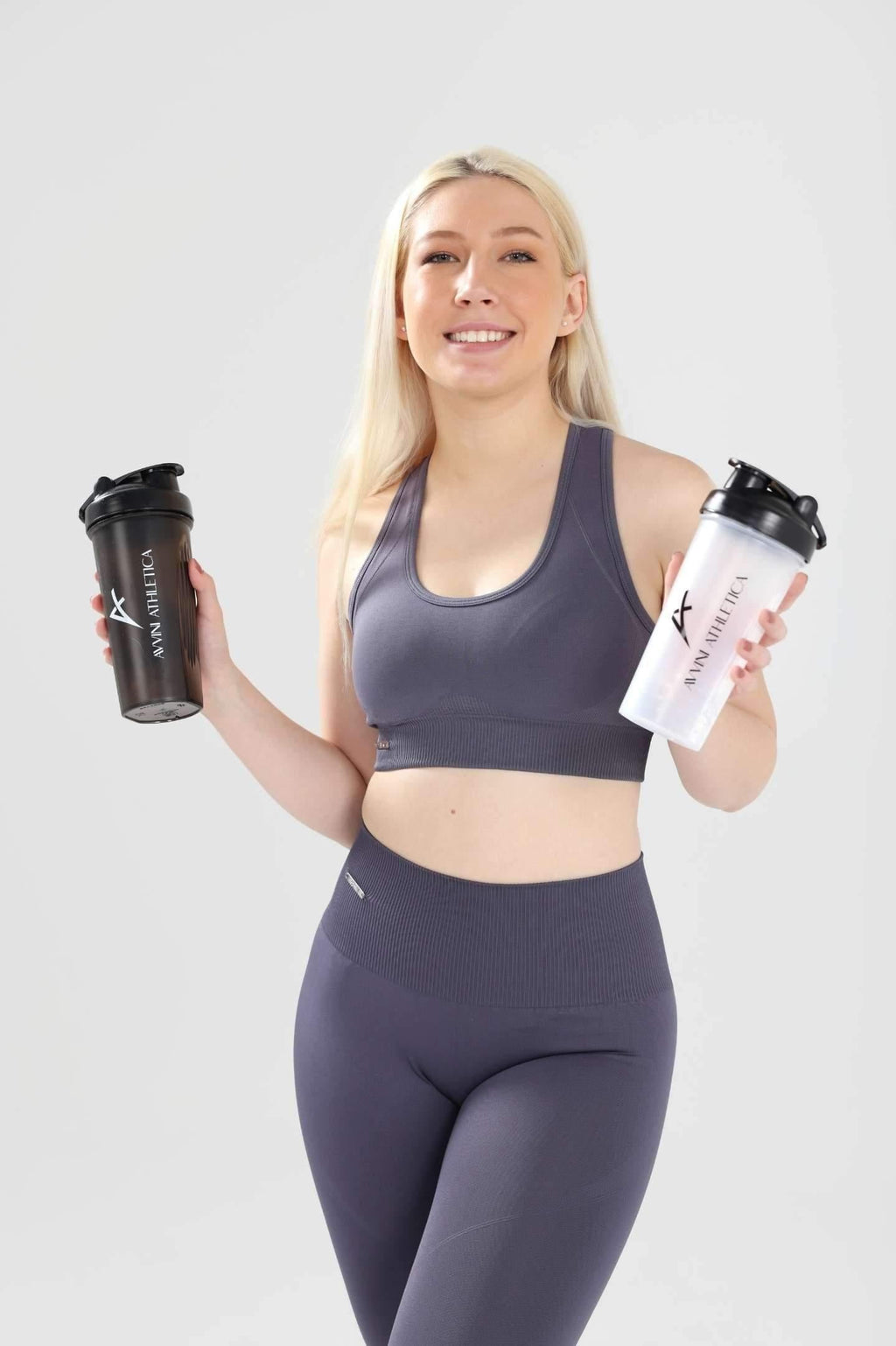 Girl smiling holding one black and one clear protein shaker bottle wearing Invictus seamless set in charcoal