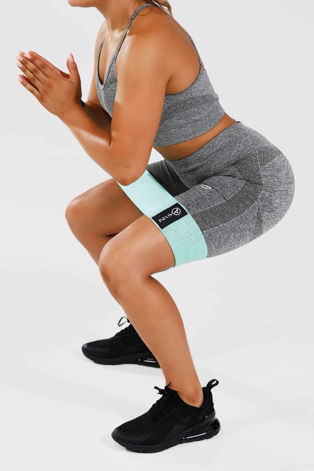 Close up girl holding squat in grey calypso seamless set wearing blue resistance band around thighs