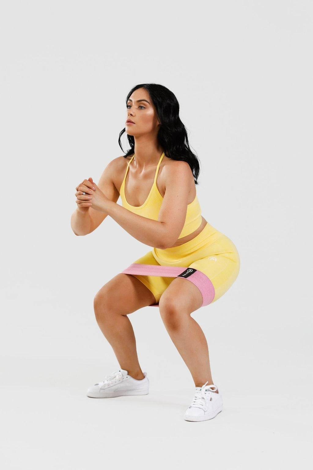 Girl holding squat wearing yellow calypso seamless set wearing pink resistance band around thighs