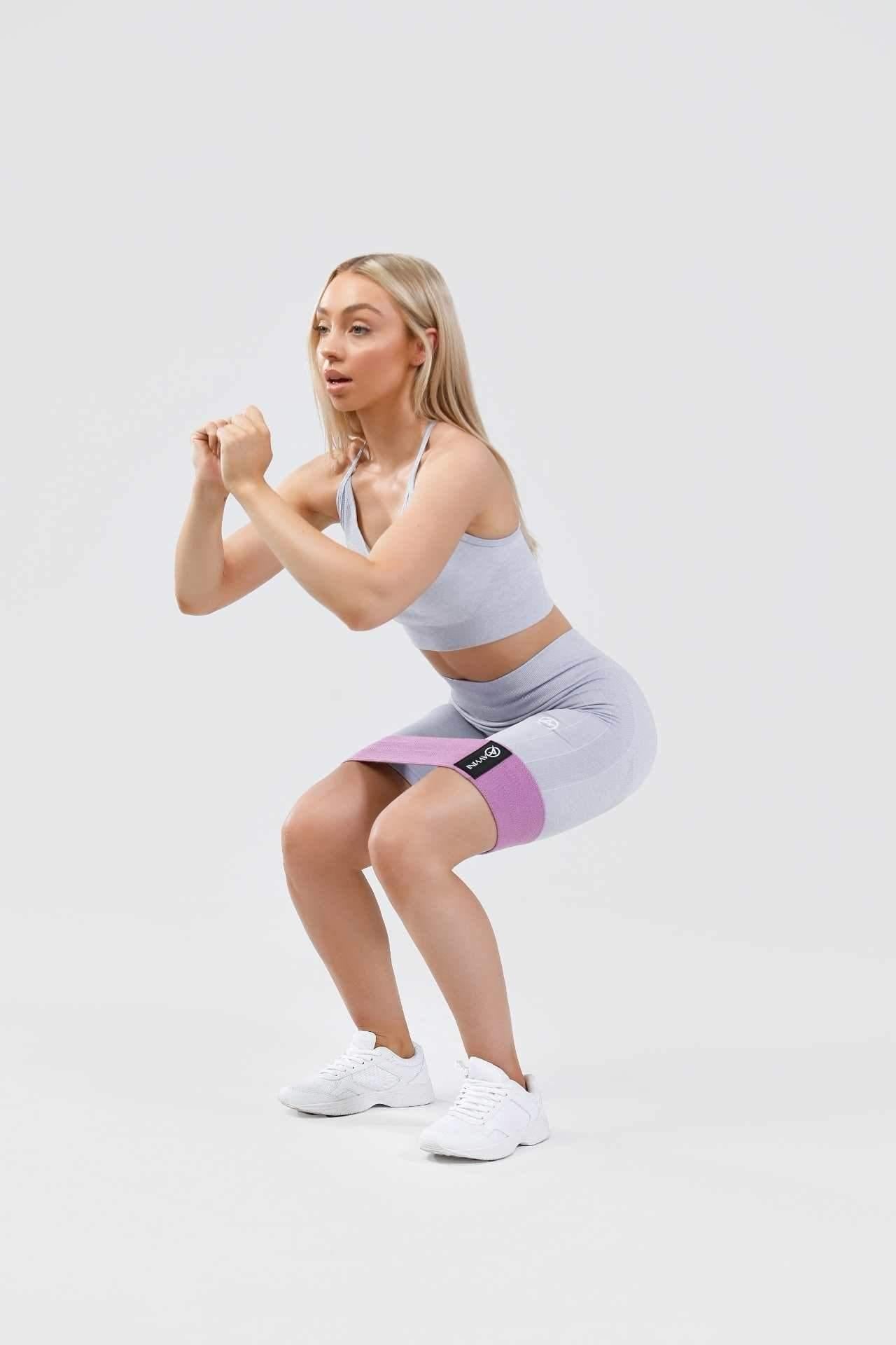 Girl holding squat wearing blue calypso seamless set, purple resistance band around thighs
